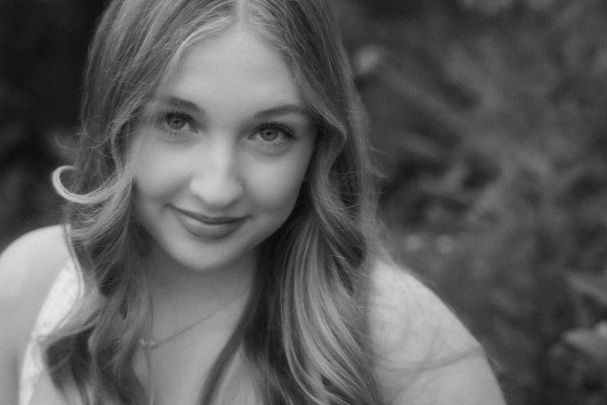 black and white upclose portrait of senior in omaha nebraska, senior has blonde hair and curls with greenery behind her at omaha castle.